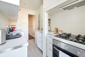 A modern kitchen with white cabinetry, a gas stove, and a kettle.