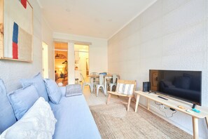 A modern living room with a sofa, TV, and a dining area with chairs and a table.