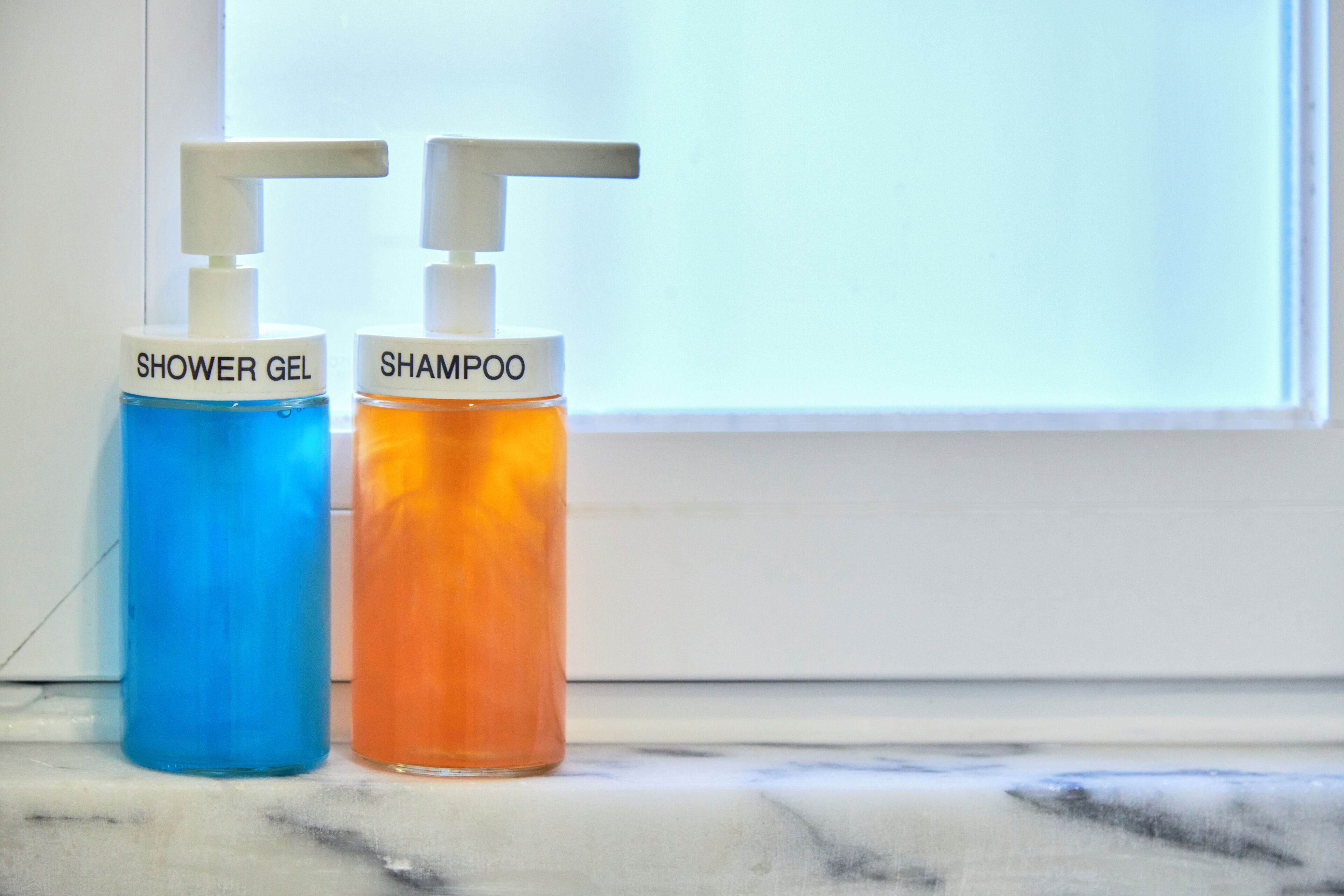 Two bottles of shower gel and shampoo on a marble surface.
