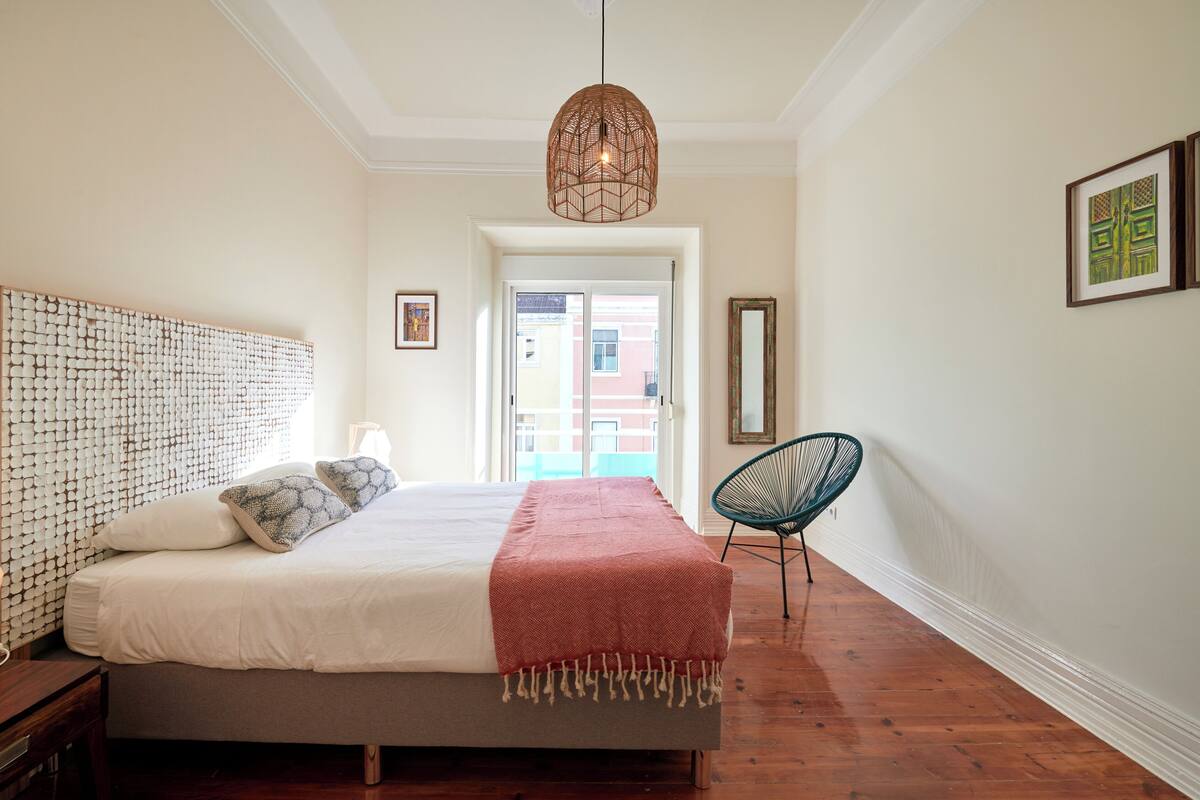 A bedroom with a bed, a hanging light fixture, a chair, and a door leading to an outdoor area.