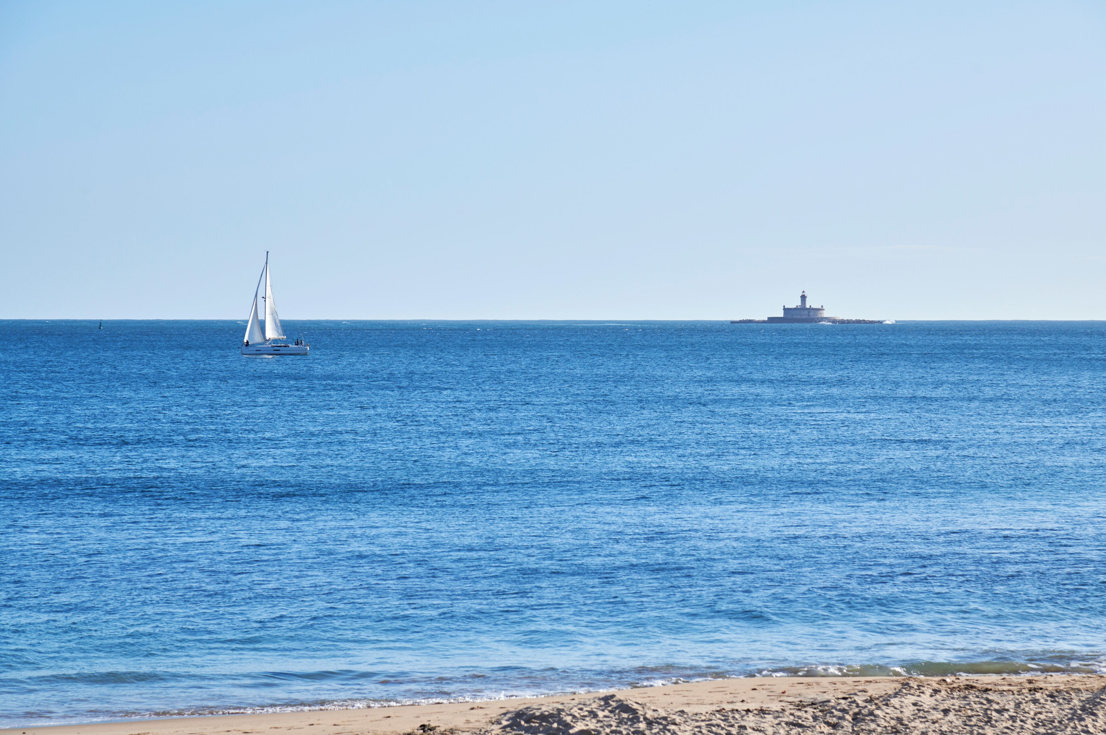 A beach with a sailboat and a lighthouse in the distance.