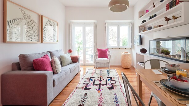 Una sala moderna con un sofá, una mesa de comedor con sillas, un tapete y una estantería con objetos decorativos.