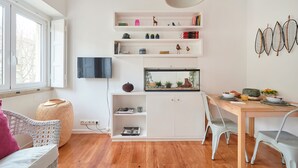 Una sala de estar moderna con televisor, estantería, mesa de comedor y un ventanal grande.