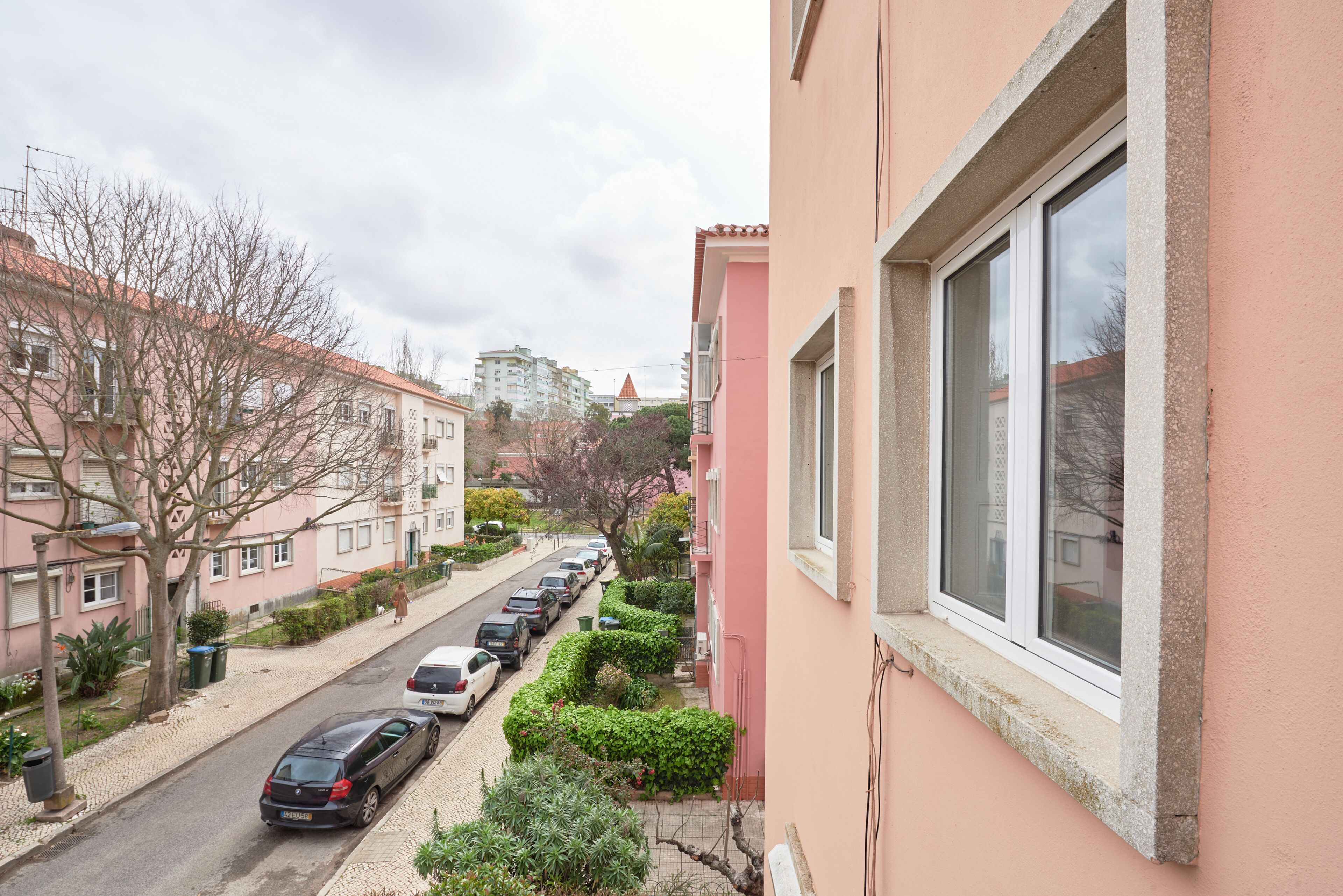 Une rue résidentielle bordée de voitures garées, un immeuble rose et un ciel dégagé.