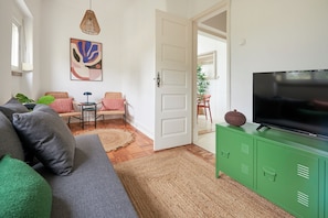 Una sala de estar con sofá, televisor, aparador verde y una puerta que da a otra habitación.