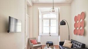 Een woonkamer met een bank, fauteuil, salontafel en een aan de muur bevestigde televisie.