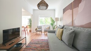 Ein Wohnzimmer mit Fernseher, einer Couch, Sesseln, einem farbenfrohen Teppich und Bildern an der Wand.