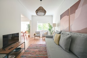 A living room with a TV, sofa, chairs, a colorful rug, and artwork on the wall.