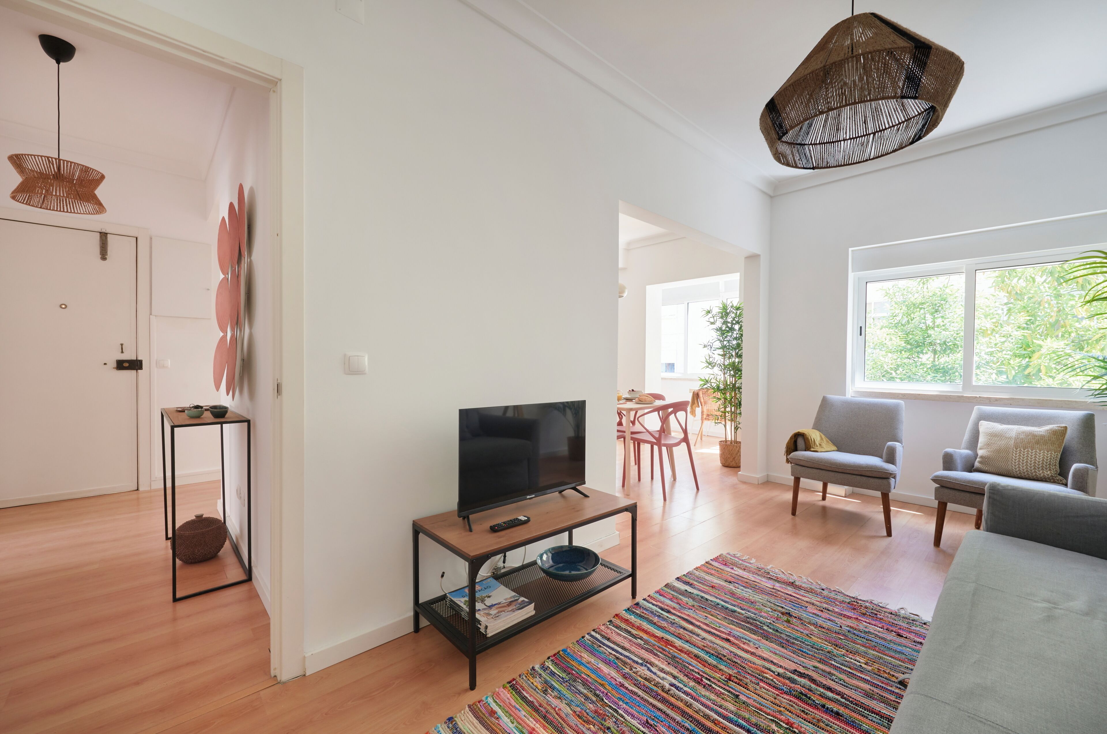 A modern living room with a television on a wooden coffee table, a colorful rug, and two grey armchairs.