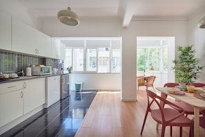 A modern kitchen with white cabinets, a black tiled backsplash, and a dining area with a table and chairs.