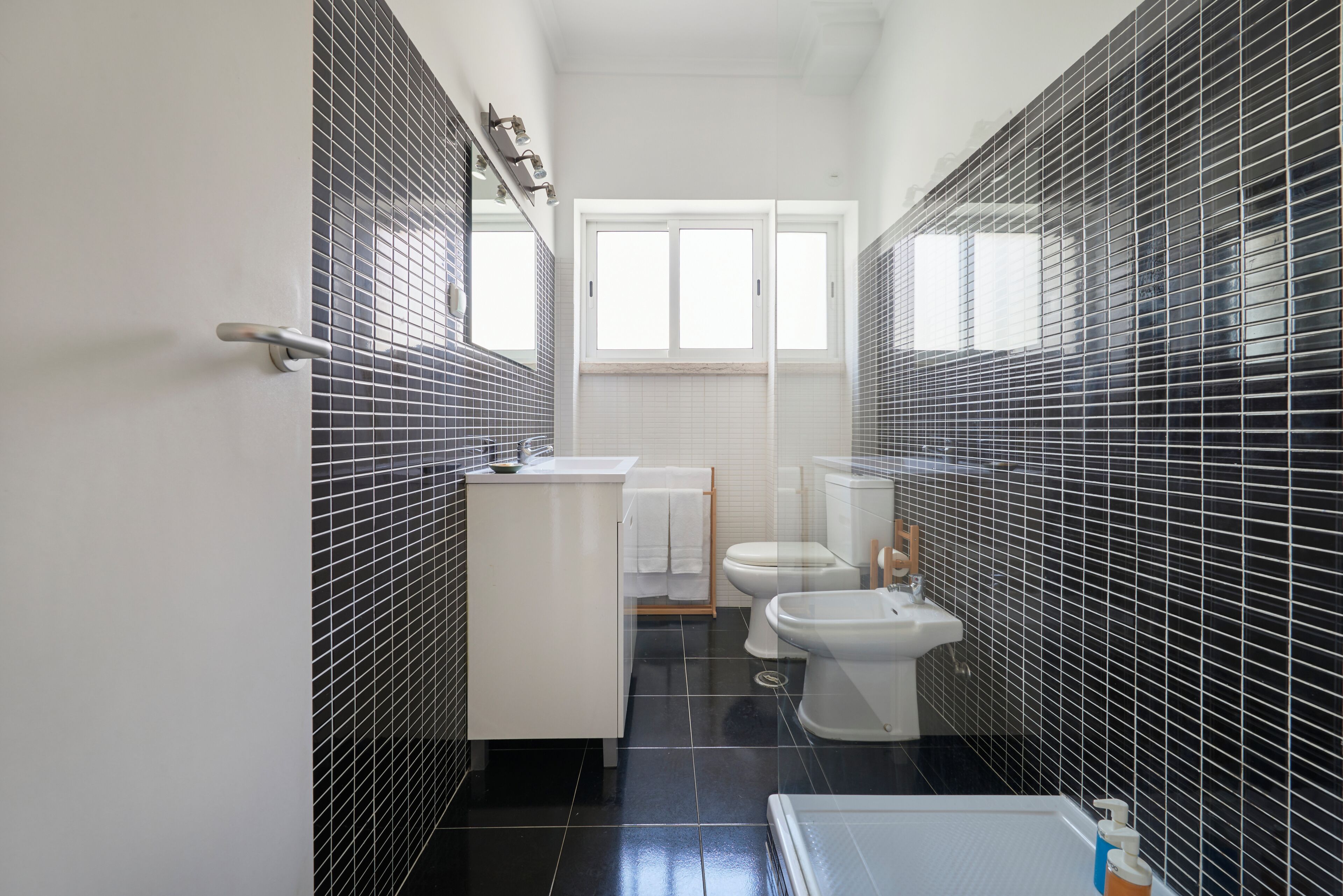 A bathroom with black tiled walls, a white sink, a toilet, and a bathtub.
