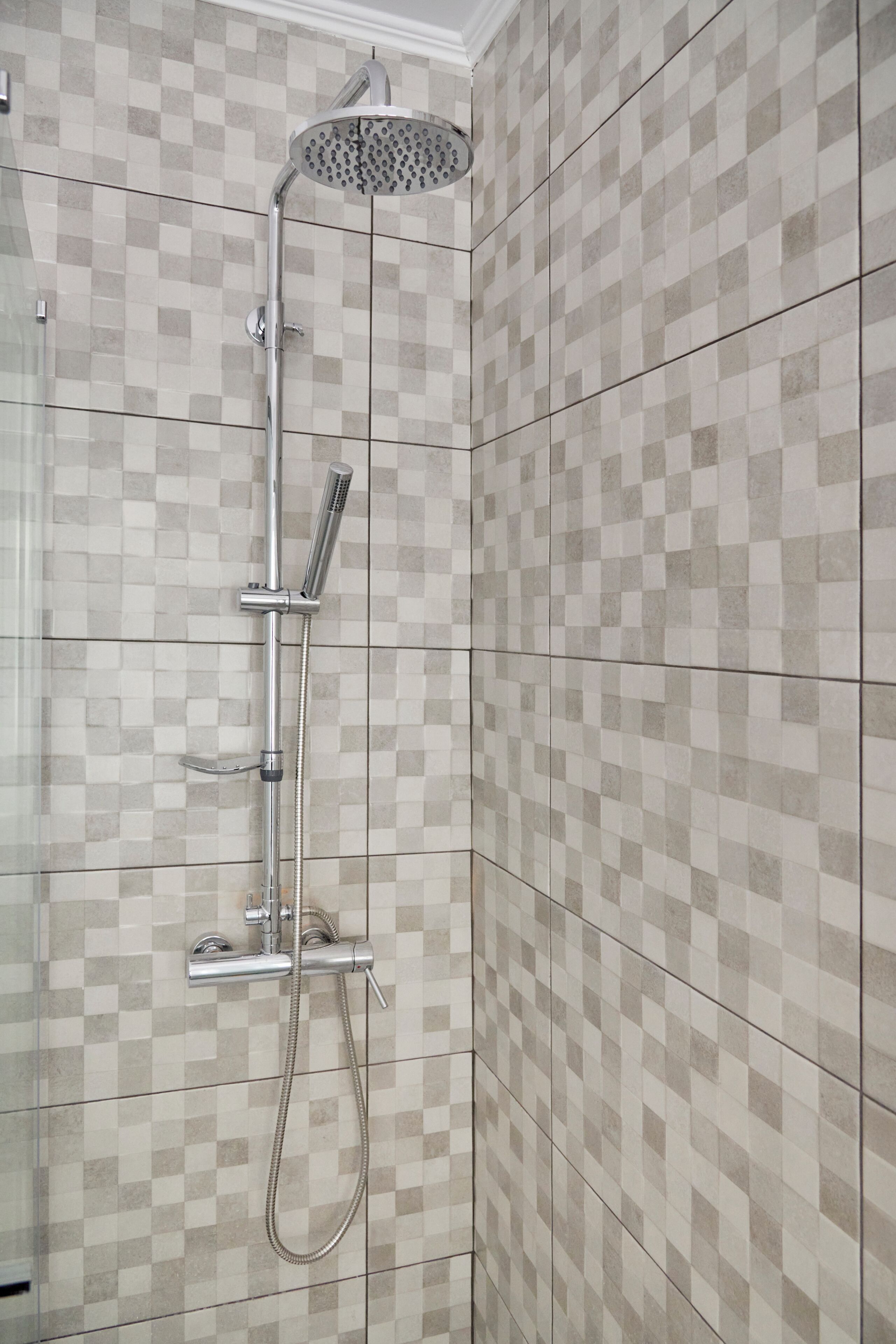 A shower with a handheld showerhead and a wall-mounted rain showerhead in a tiled bathroom.