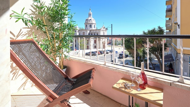 A balcony with a chair, a small table with a bottle and glasses, and a view of a building with a dome. - Enjoy The Sunny Balcony, By Timecooler (Lisbon)