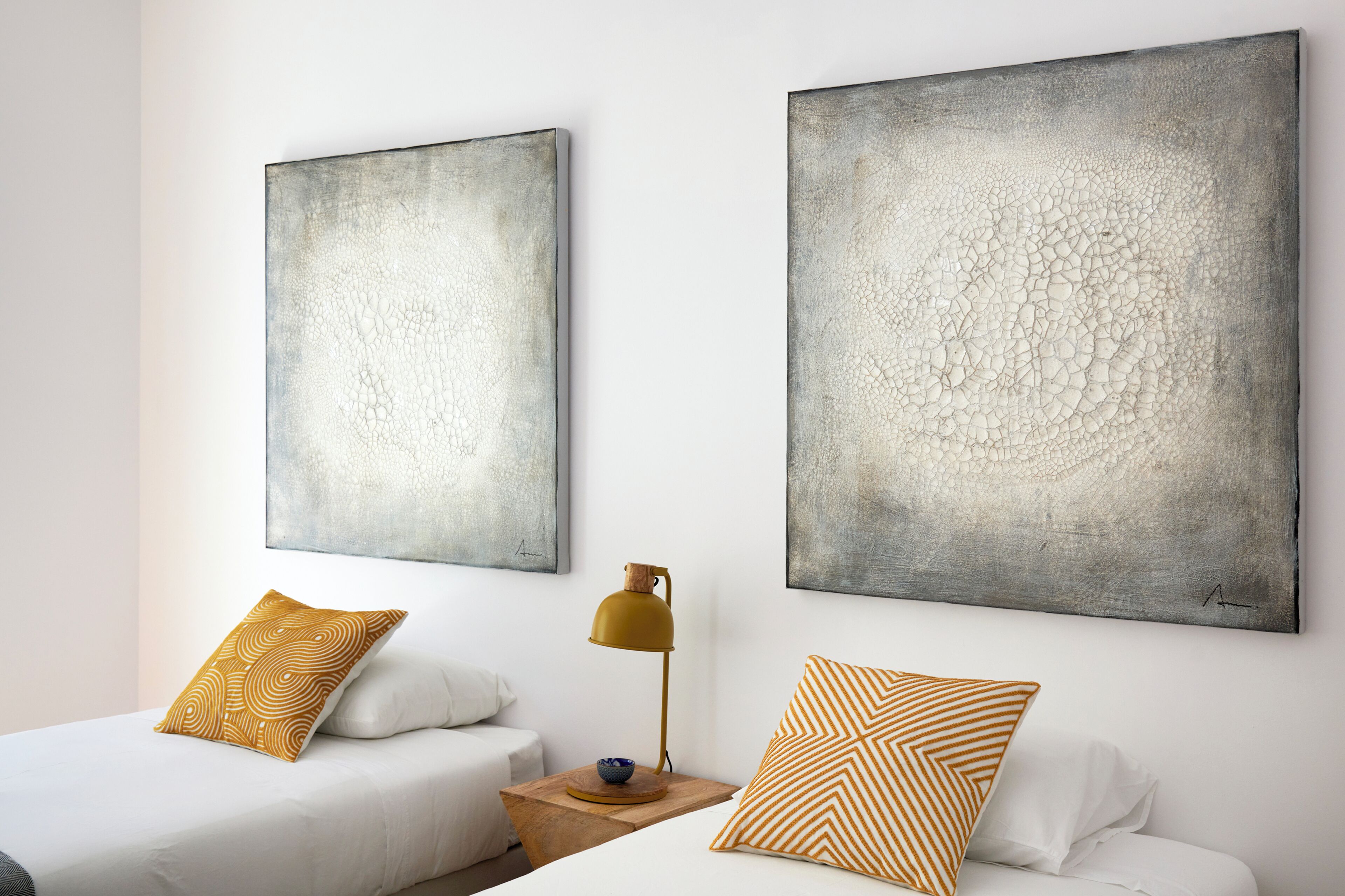 Une chambre d’hôtel avec deux lits, une table de chevet, une lampe et deux tableaux abstraits accrochés au mur.