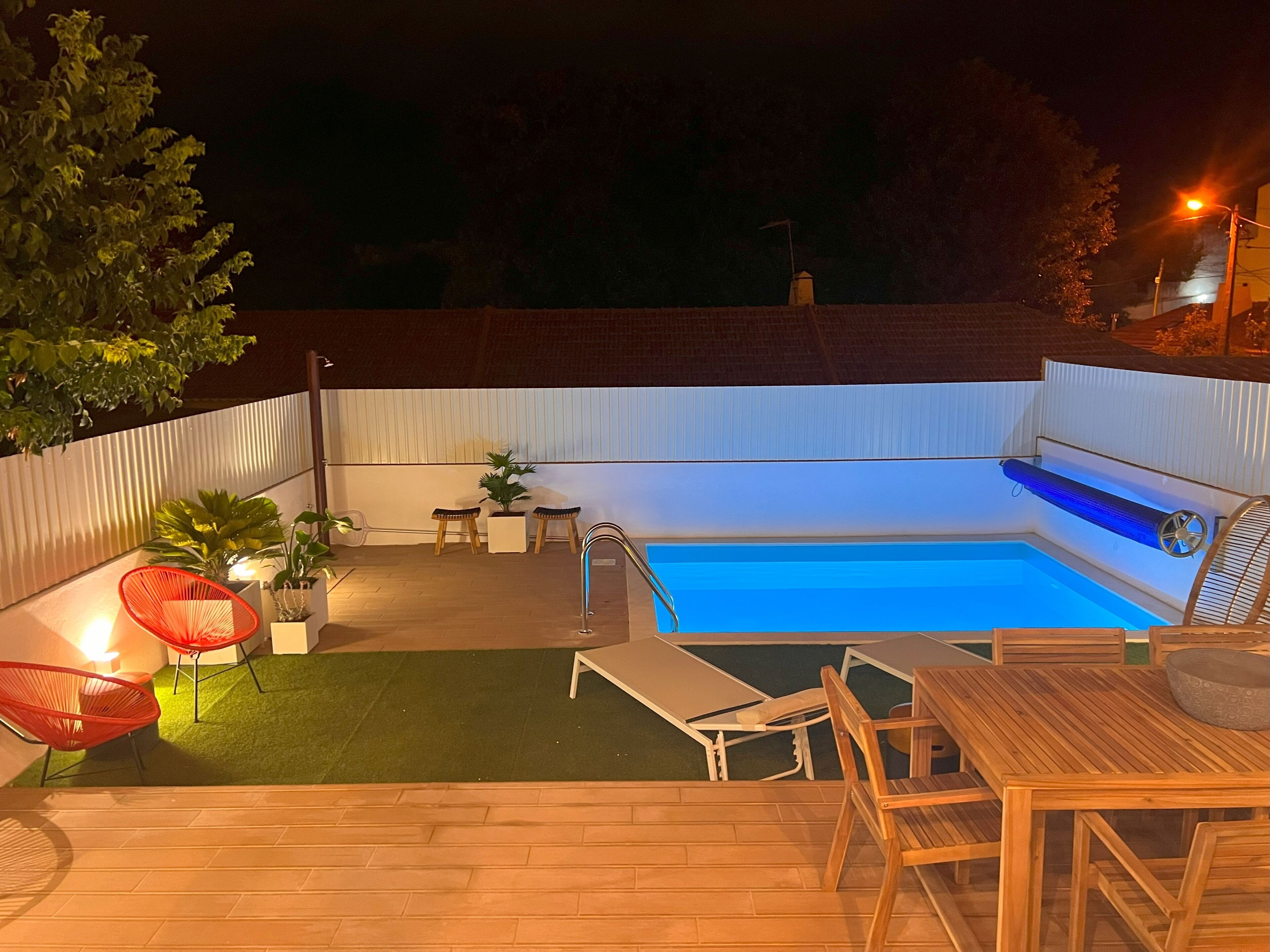A backyard with a swimming pool, wooden deck, and outdoor furniture.