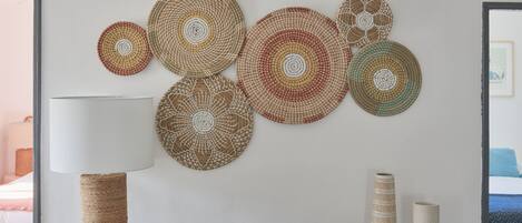 Une pièce avec une table en bois, une lampe et des éléments décoratifs en forme d’œuvres d’art murales tissées.