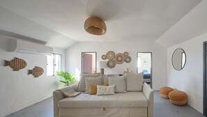 A spacious living room with a beige sofa, a woven ceiling light, wall-mounted fish decorations, and a large mirror. - Comporta Sandy Villa, By Timecooler (Alcacer do Sal)