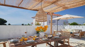 An outdoor dining area with a table set for breakfast, surrounded by wicker furniture and a large umbrella. - Comporta Sandy Villa, By Timecooler (Alcacer do Sal)