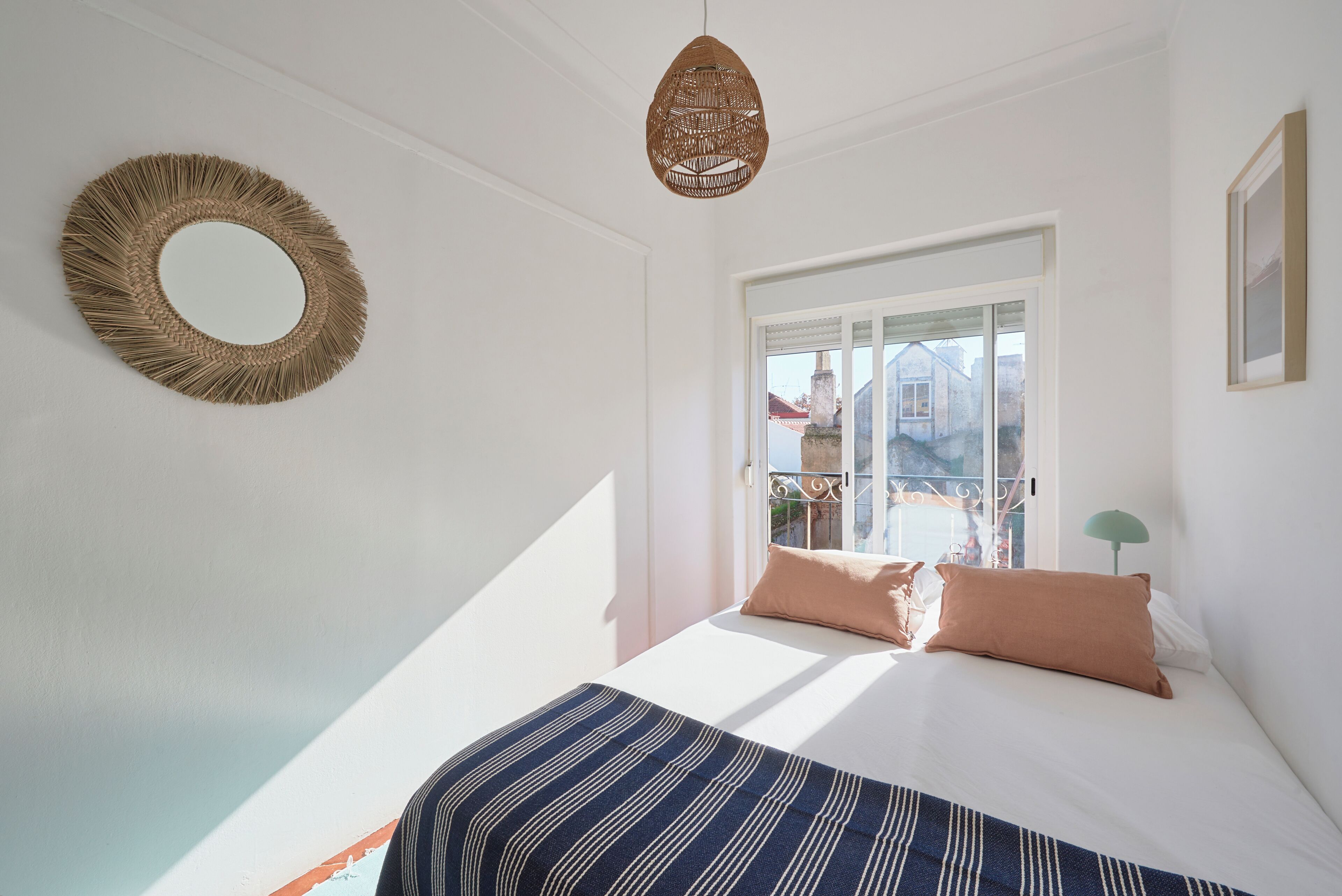 Un dormitorio con cama, ventana, lámpara colgante y espejo en la pared.