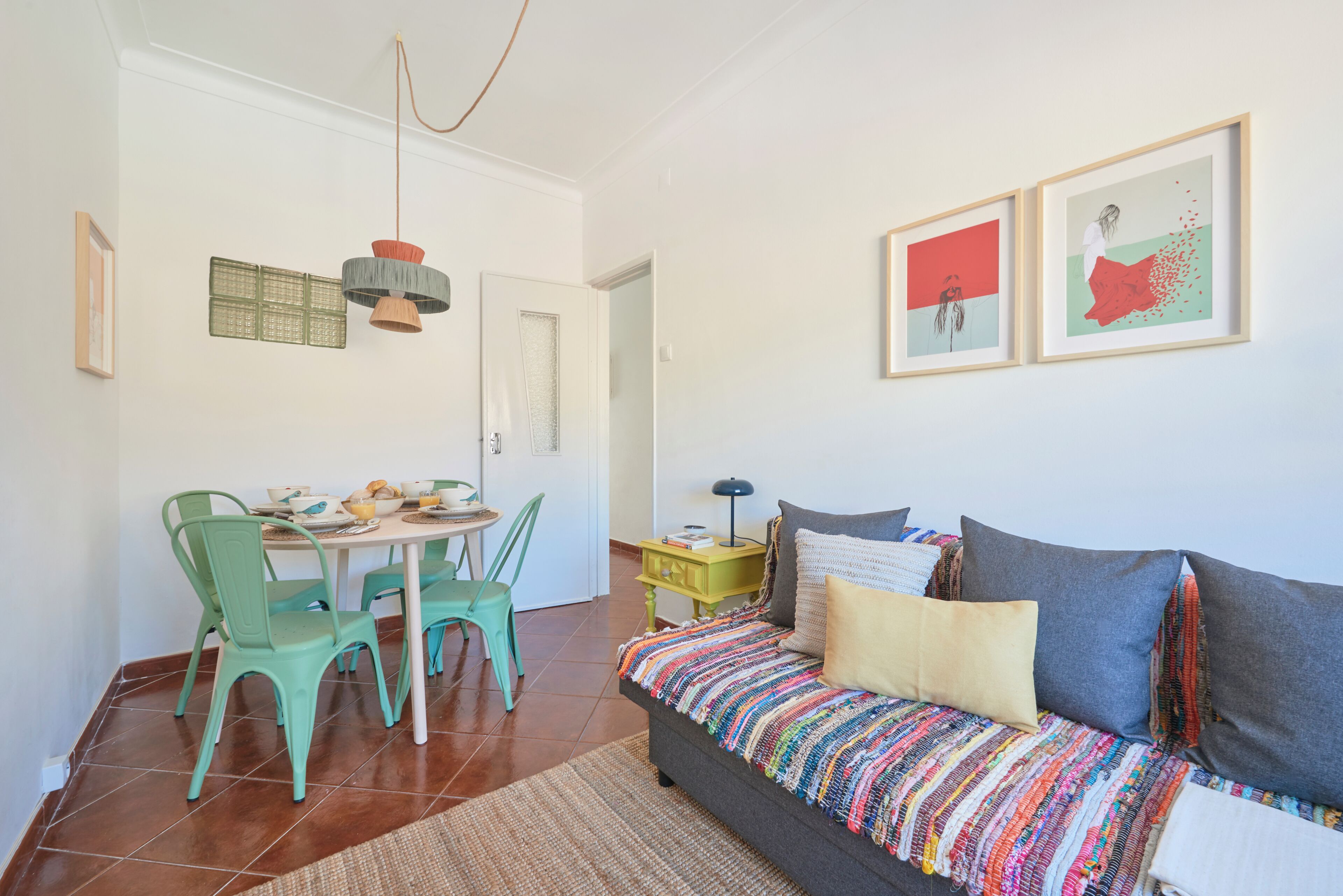 A living room with a sofa, a dining table with chairs, and artwork on the walls.
