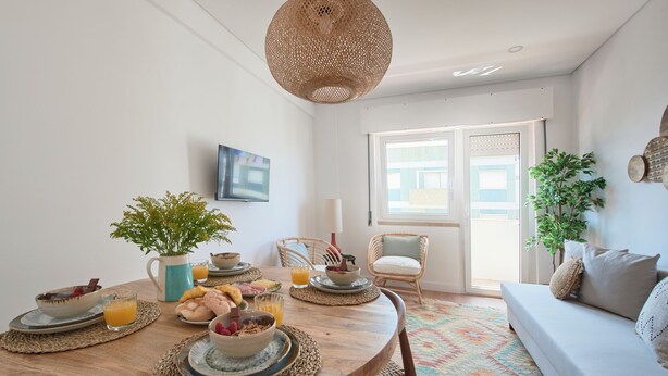 A dining area with a round wooden table, wicker chairs, and a sofa. - Sunset Bay View Renovated Apt, By Timecooler (Setubal)