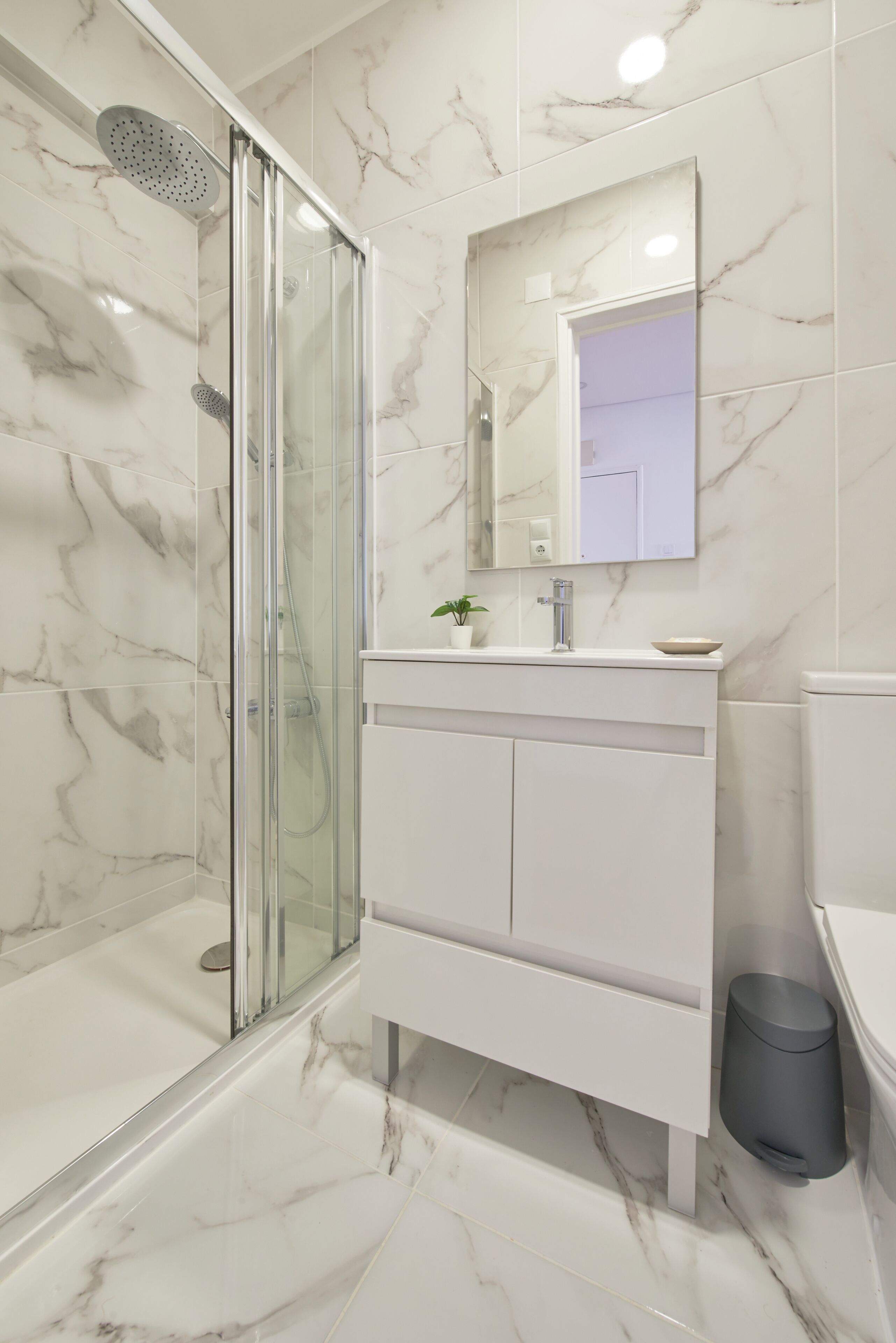 Une salle de bain moderne avec une douche à parois de verre, un meuble-lavabo blanc avec un miroir et un revêtement de sol en marbre.