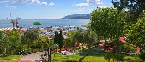 A coastal park with a playground, walking paths, and a view of the sea and distant buildings.