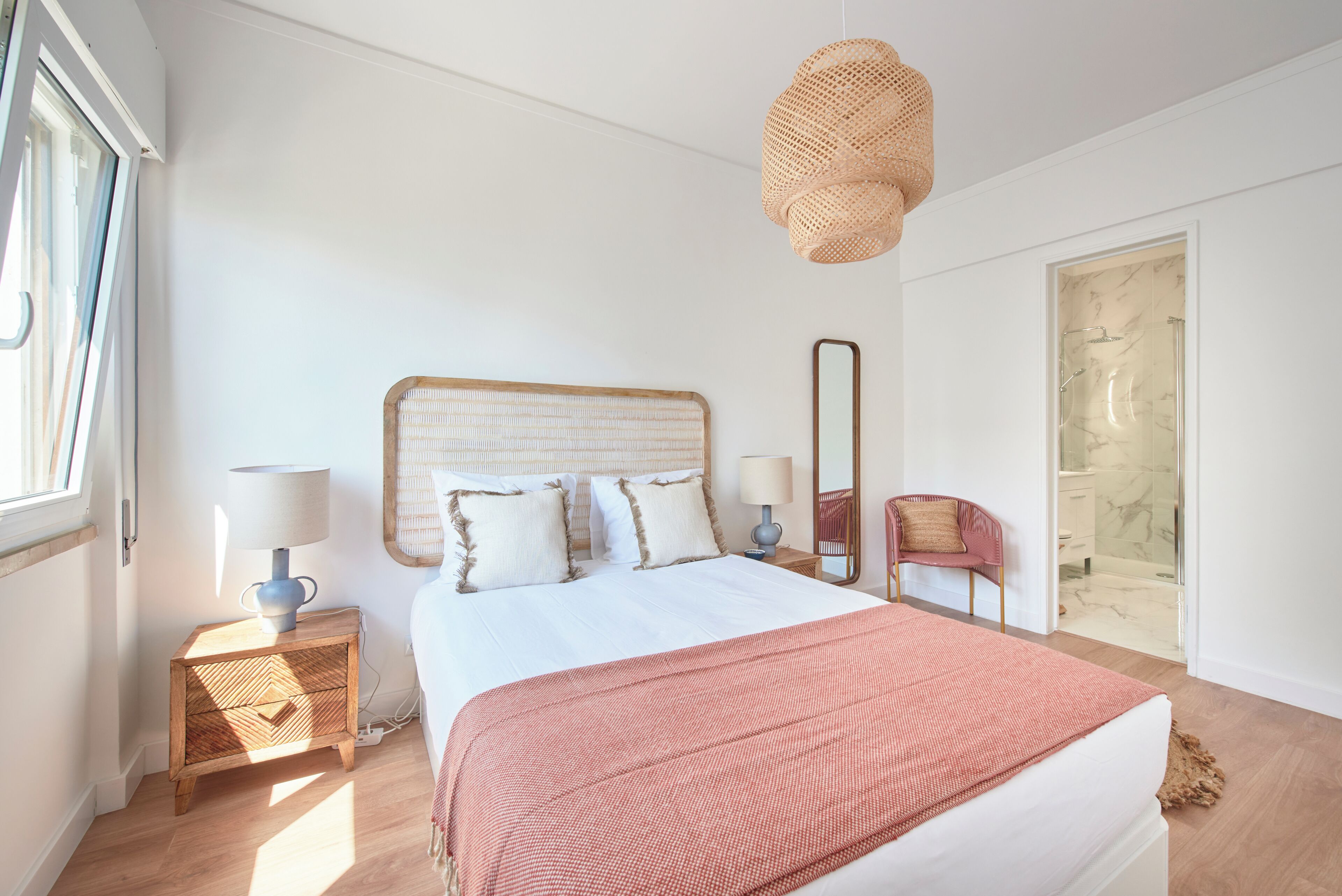 Quarto com cama, luminárias de cabeceira, espelho, cadeira e área de chuveiro.