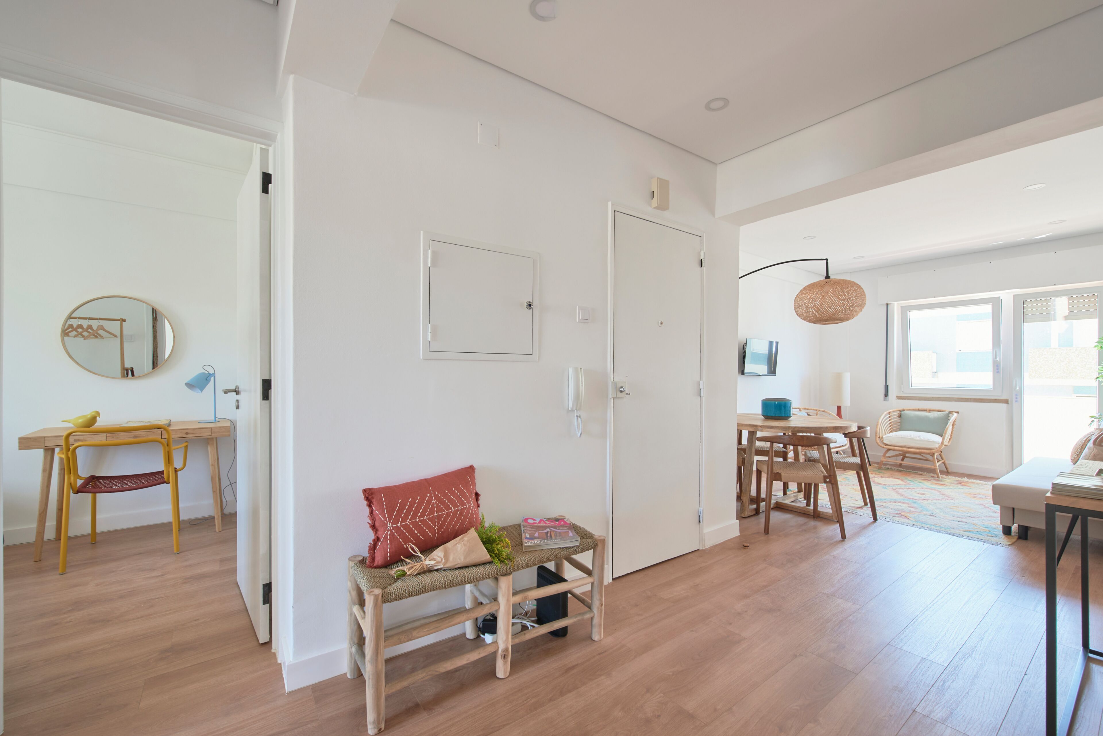 Amplia habitación con piso de madera, un comedor con mesa y sillas, un banco con cojines y una puerta con espejo.