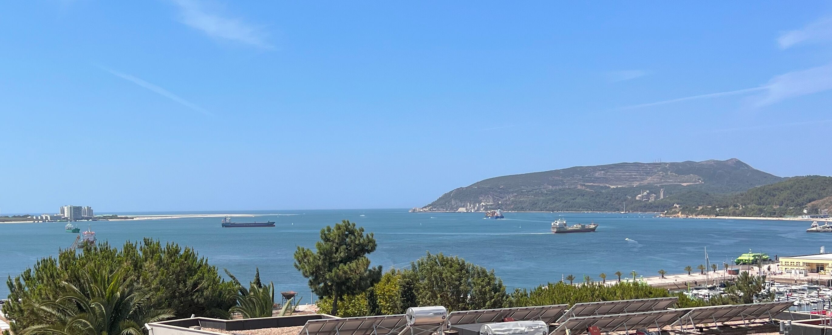 A coastal view with ships, a mountain, and solar panels.