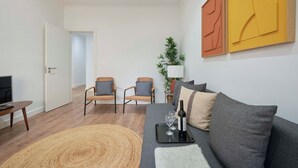 A modern living room with a sofa, two armchairs, a coffee table, a TV, a plant, and abstract wall art. - Spacious & Light Filled 4Br Apartment By Timecoler (Amadora)