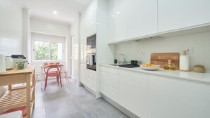 A modern kitchen with white cabinetry, a wooden dining table, and a window providing natural light. - Spacious & Light Filled 4Br Apartment By Timecoler (Amadora)