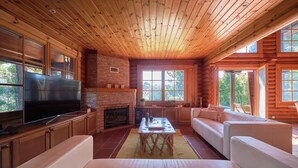 A log cabin interior with a TV, fireplace, sofa, and large windows. - Beach & Golf Retreat W Amazing Pool, By Timecooler (Almada)