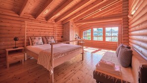 A log cabin bedroom with a wooden bed, a bench with towels, a nightstand, and a window with a view. - Beach & Golf Retreat W Amazing Pool, By Timecooler (Almada)
