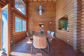 L’intérieur d’une cabane en rondins, avec une table à manger, des chaises, un luminaire suspendu et une grande fenêtre.