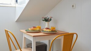 Un comedor con una mesa y dos sillas, un florero con flores y una ventana con luz natural.
