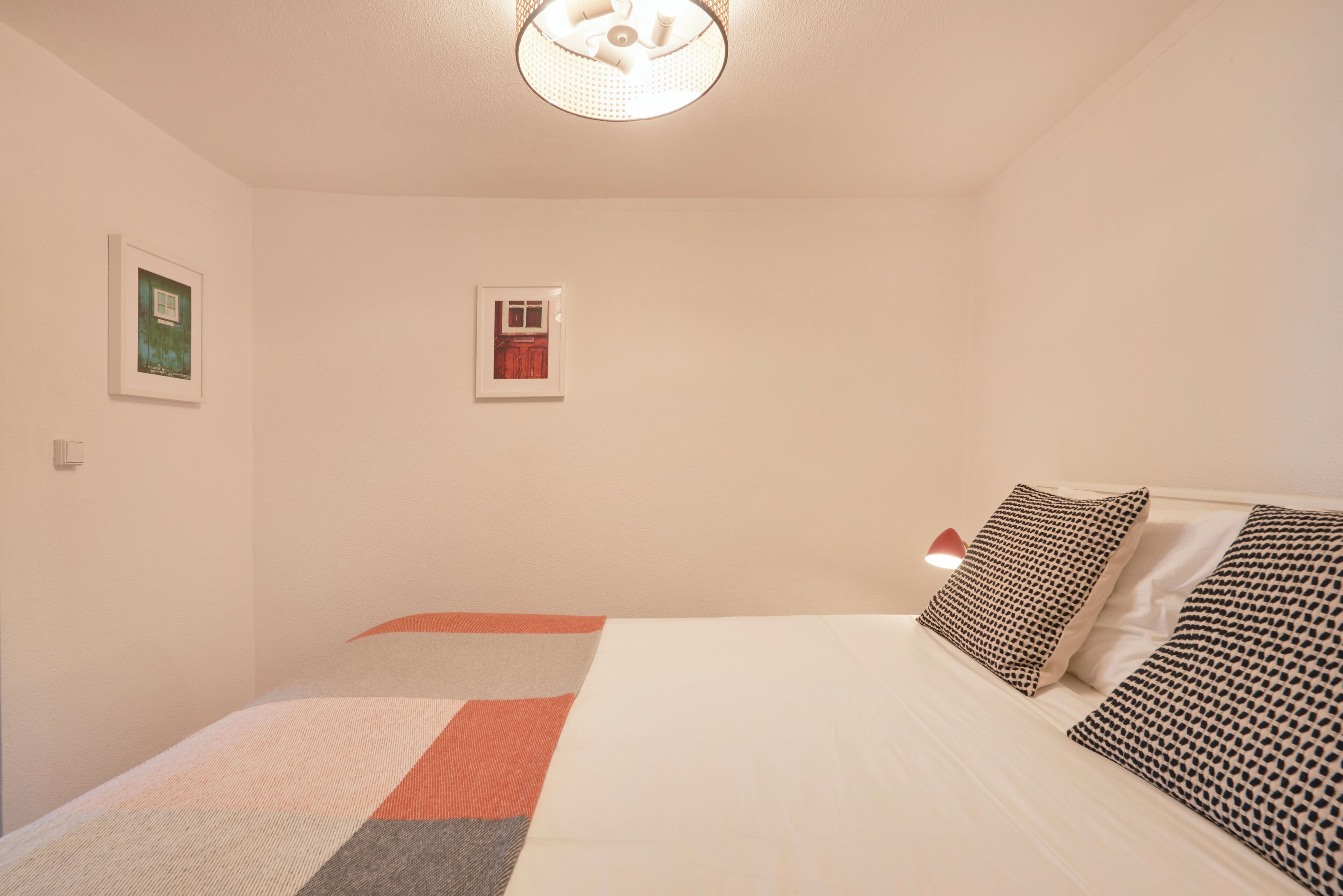 Ein Schlafzimmer mit einem Bett, Kissen, einer Wandleuchte und zwei gerahmten Bildern.