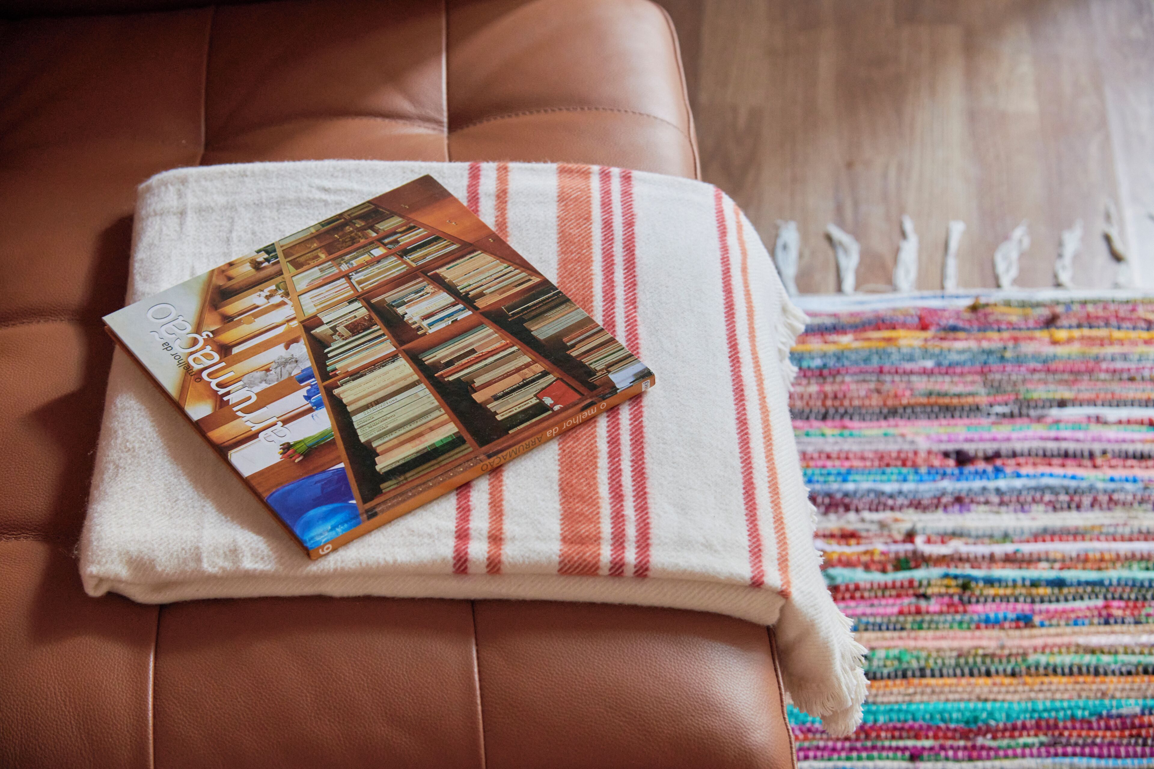 A brown leather couch with a magazine and a striped towel on it.
