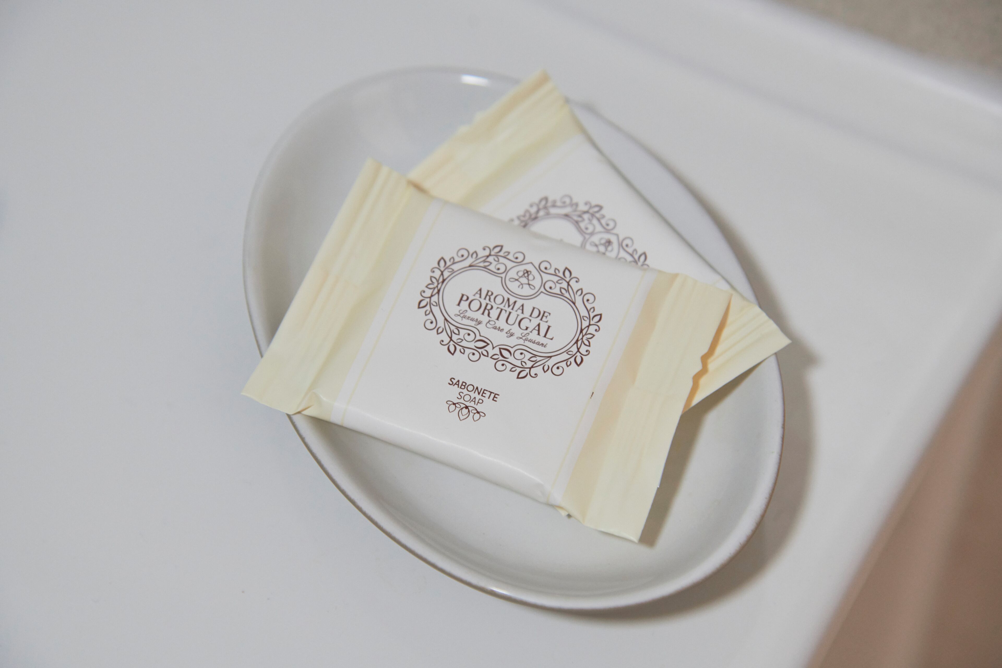 Un plat blanc amb una barra de sabó etiquetada com 'AROMA DE PORTUGAL' i 'SABONETE SOAP'.