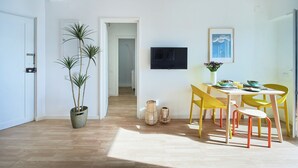 A modern interior with a dining area, a TV mounted on the wall, and a hallway leading to another room. - Seaview & Sunset Balcony Charm, By Timecooler (Setubal)