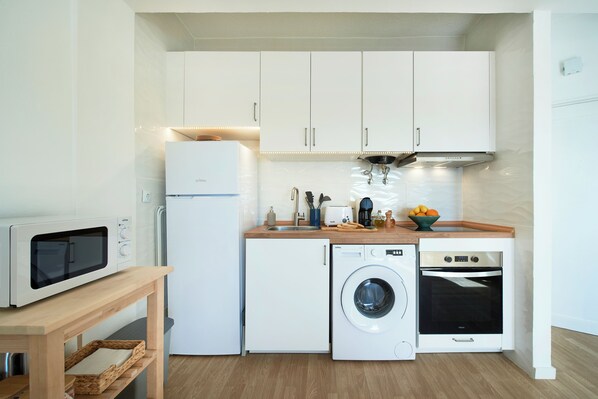 Una cocina compacta con microondas, lavadora y horno, junto con una mesa de madera y un lavabo.