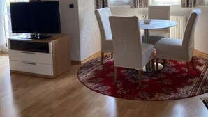 A room with a wooden ceiling, a television on a cabinet, a dining table with chairs, and a red patterned rug. - Holiday Apartment Schupp (Dachsberg)