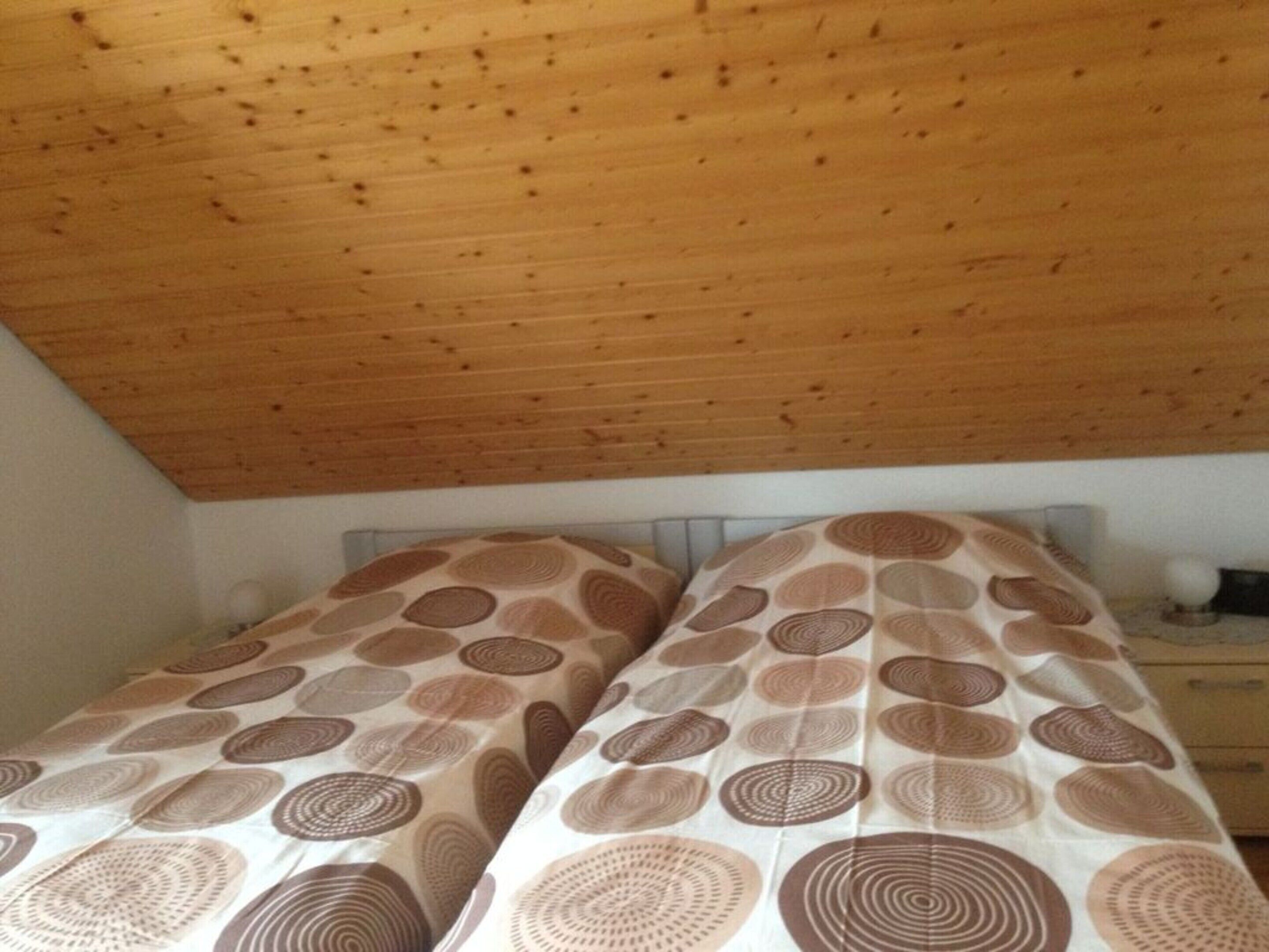 Une chambre à coucher avec un plafond en bois et un lit recouvert d’une literie à motifs.