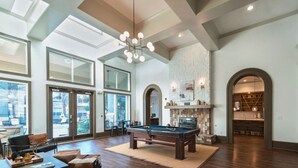 Una habitación amplia con mesa de billar, ventanas grandes y chimenea.