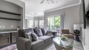 Una sala de estar moderna con un sofá gris, una mesa de centro de vidrio y un televisor montado en la pared.