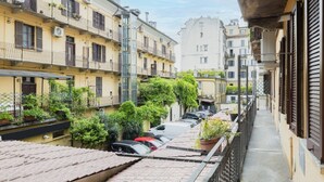 Un vialetto stretto fiancheggiato da edifici, con balconi adornati da piante e una fila di auto parcheggiate.