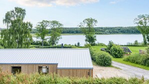 A modern building with a metal roof, surrounded by lush greenery and a lake in the background. - 4 Star Holiday Home in Ronde (Ronde)