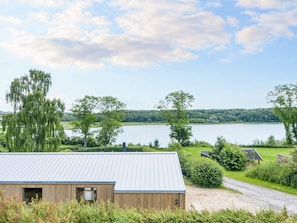 A modern building with a metal roof, surrounded by lush greenery and a lake in the background. - 4 Star Holiday Home in Ronde (Ronde)