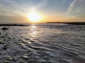 Uma praia com o sol se pondo sobre a água, criando uma atmosfera calma e serena.