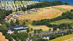 Eine Vogelperspektive zeigt eine Küstenwohngegend mit mehreren Wohneinheiten, einem Schwimmbadkomplex und einem großen, offenen Rasenfeld.
